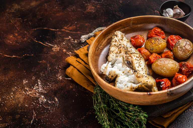 baked halibut fish with roasted tomato and potato in wooden plat