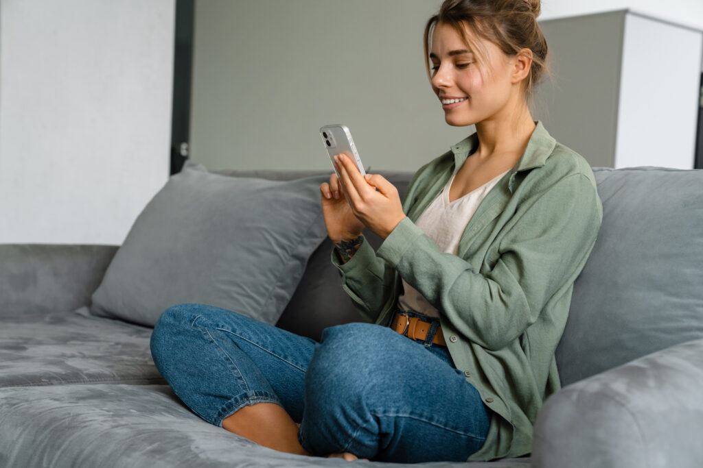 happy nice woman using mobile phone while sitting on sofa