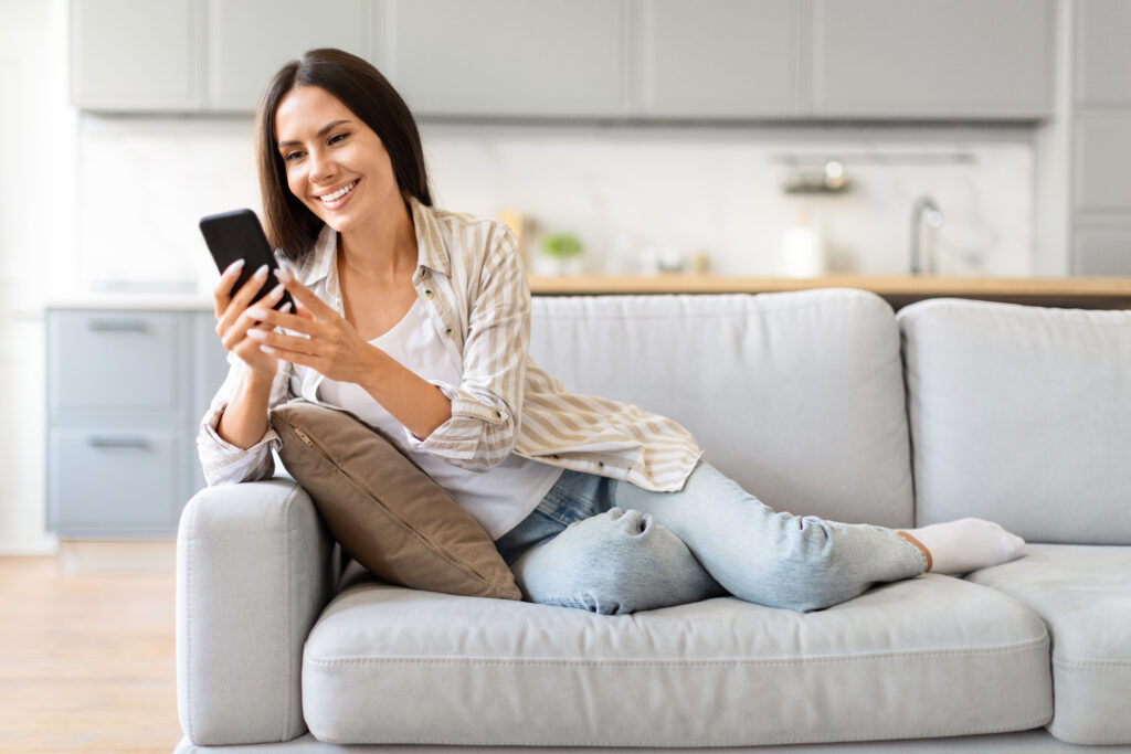 happy woman browsing phone on couch at home