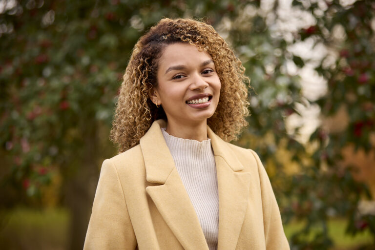 portrait of smiling young woman wearing coat standing outside in winter or autumn countryside
